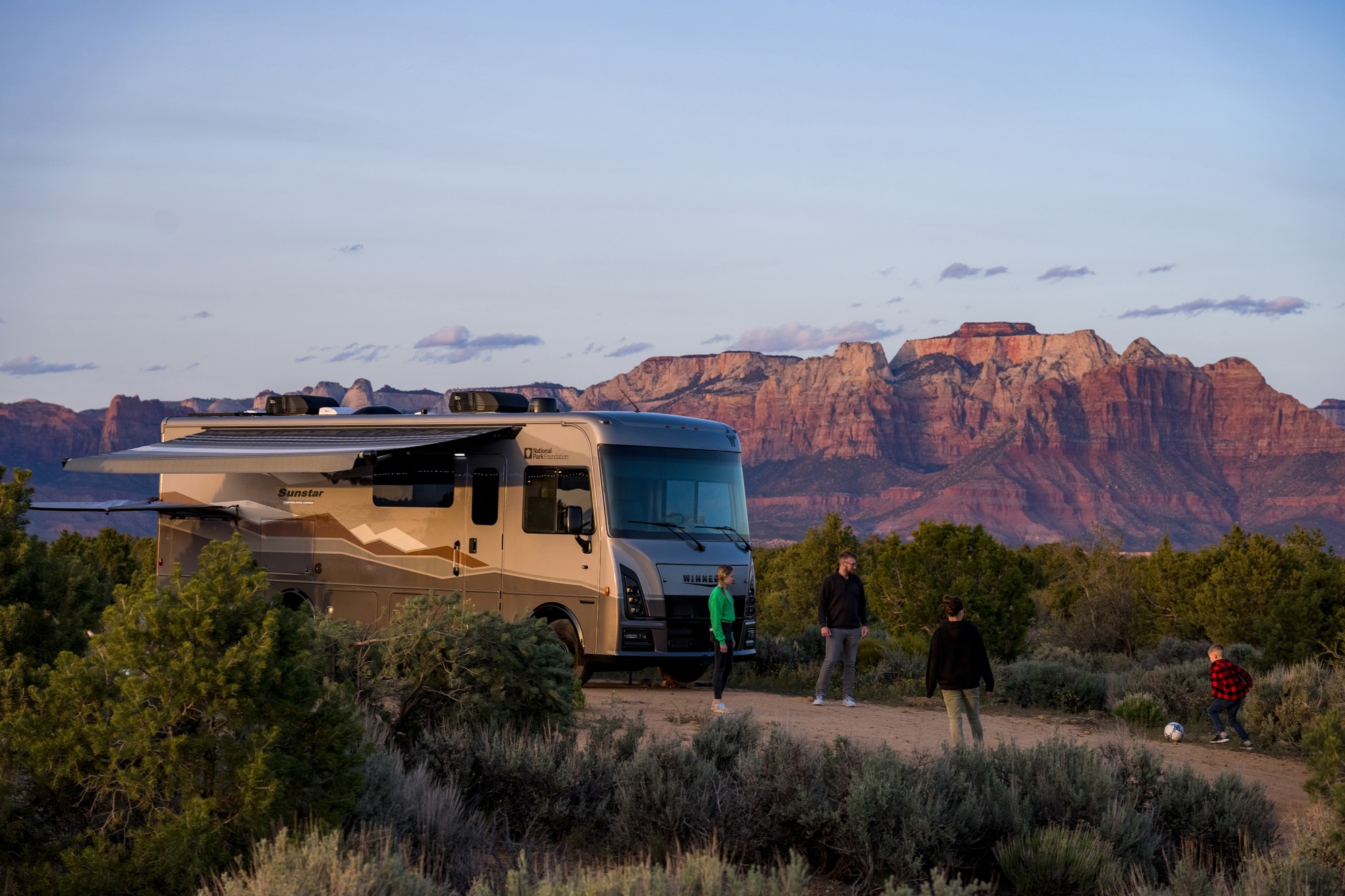 RV_Lifestyle_Winnebago SS NPF-LS set up at rural campsite with family of 4 playing soccer in front of unit.jpg